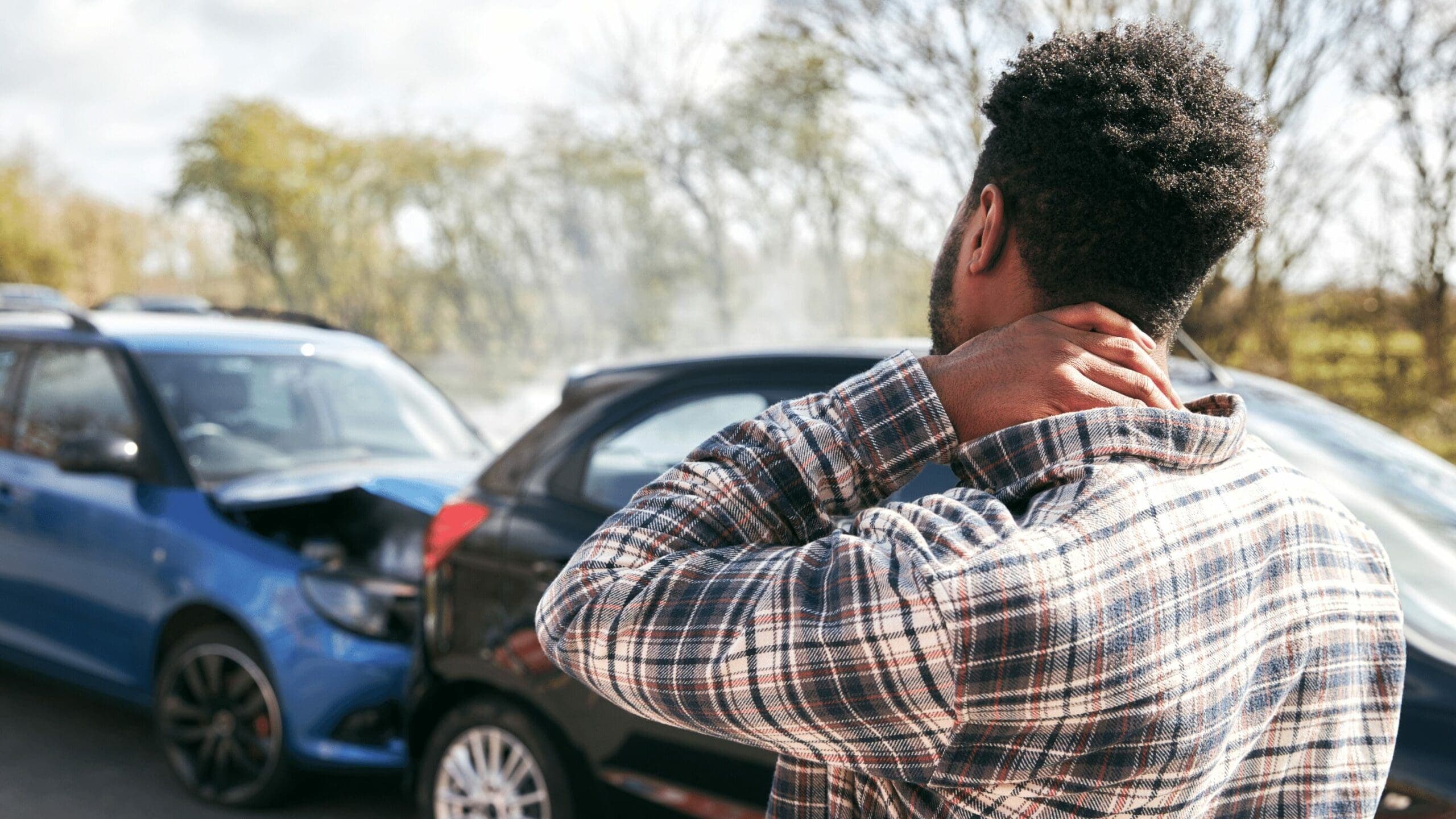 Injured man clutching neck, gazing at accidental car