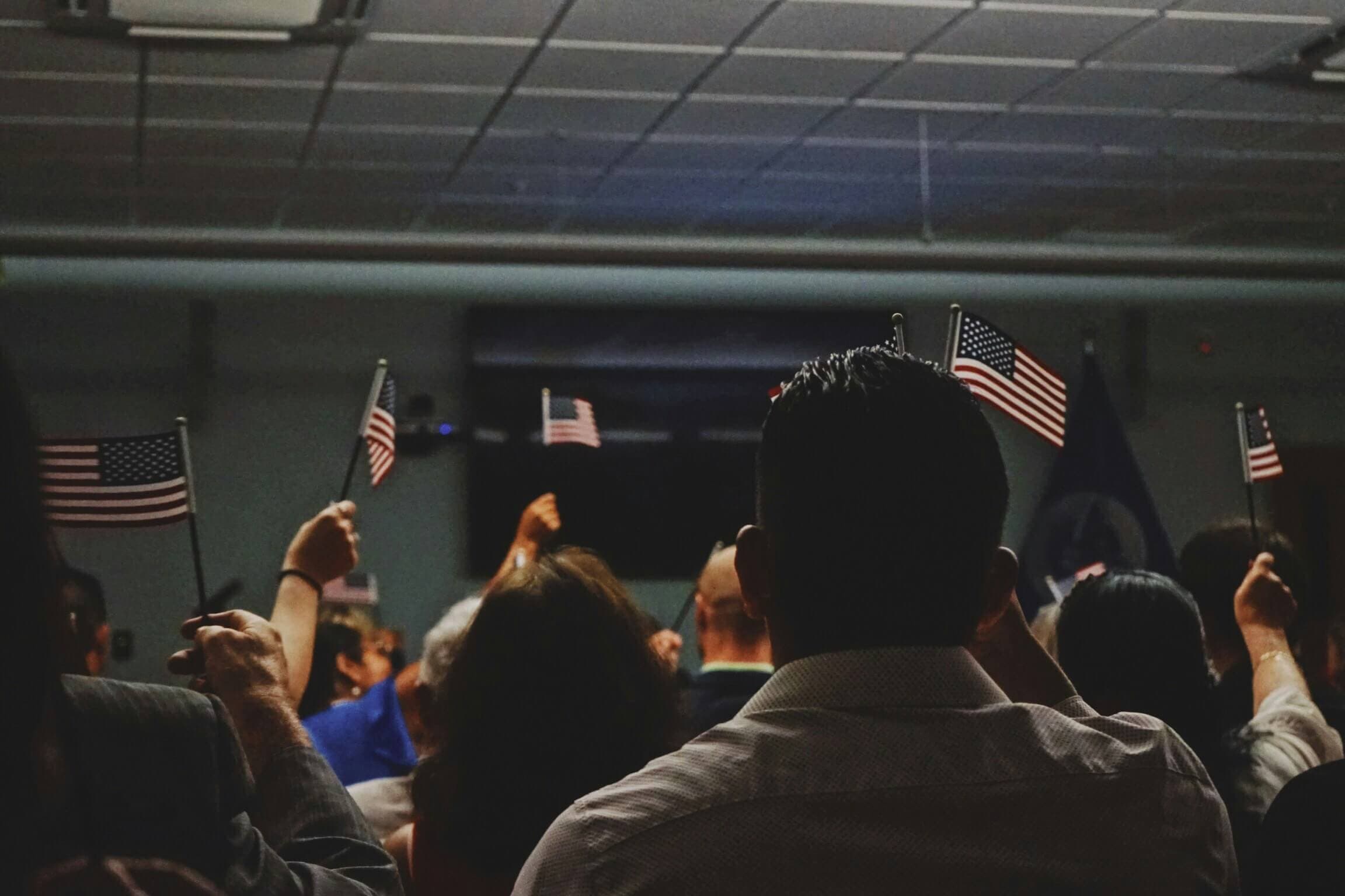 People holding small American flags during a citizenship or immigration-related event, representing lawful permanent resident status in the United States.
