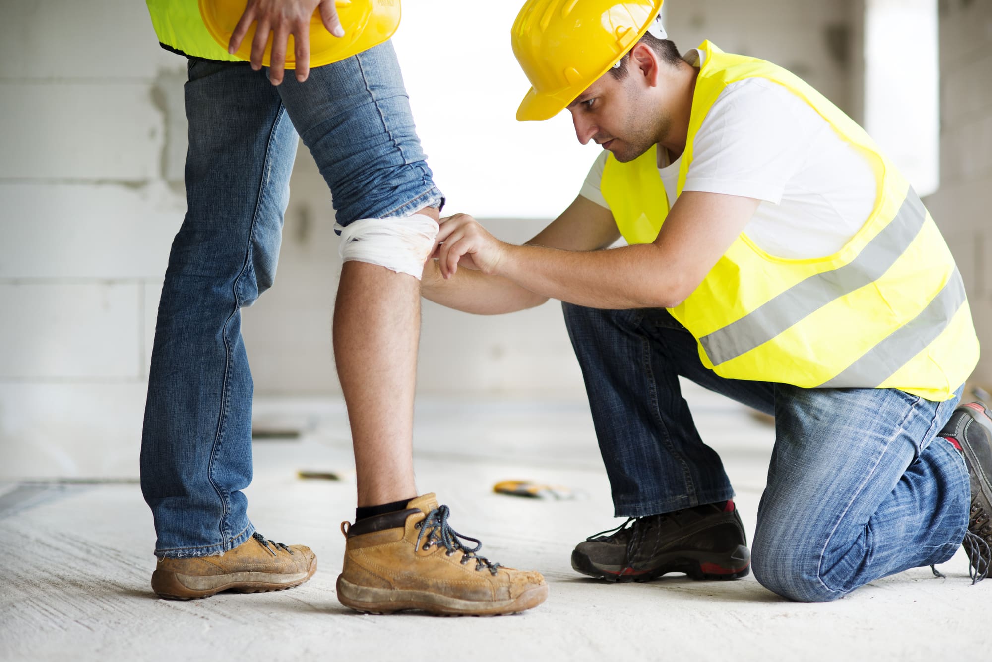 A man in a hard hat and yellow vest assisting another injured man. A case of worker's compensation