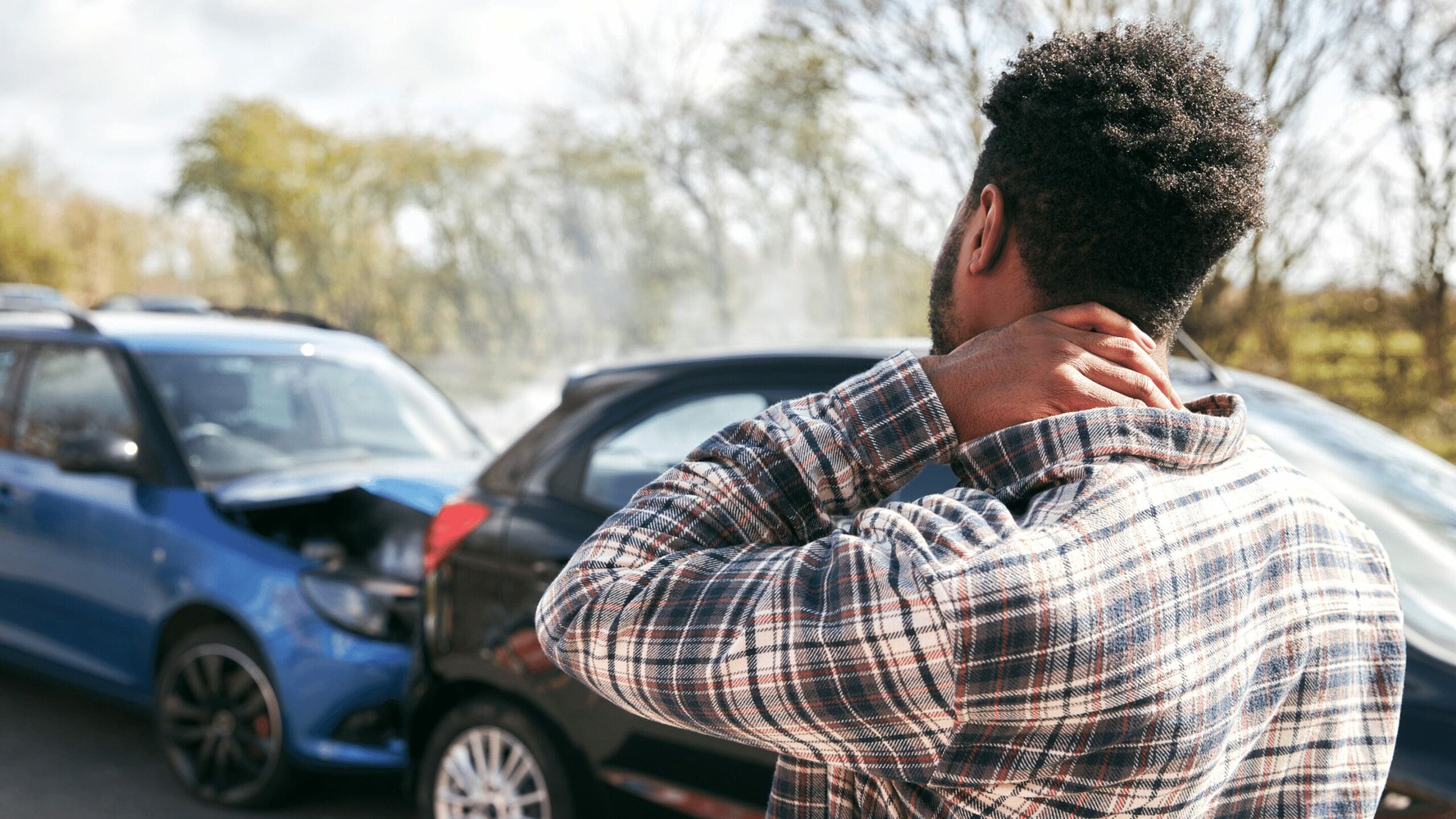 Injured man clutching neck, gazing at accidental car