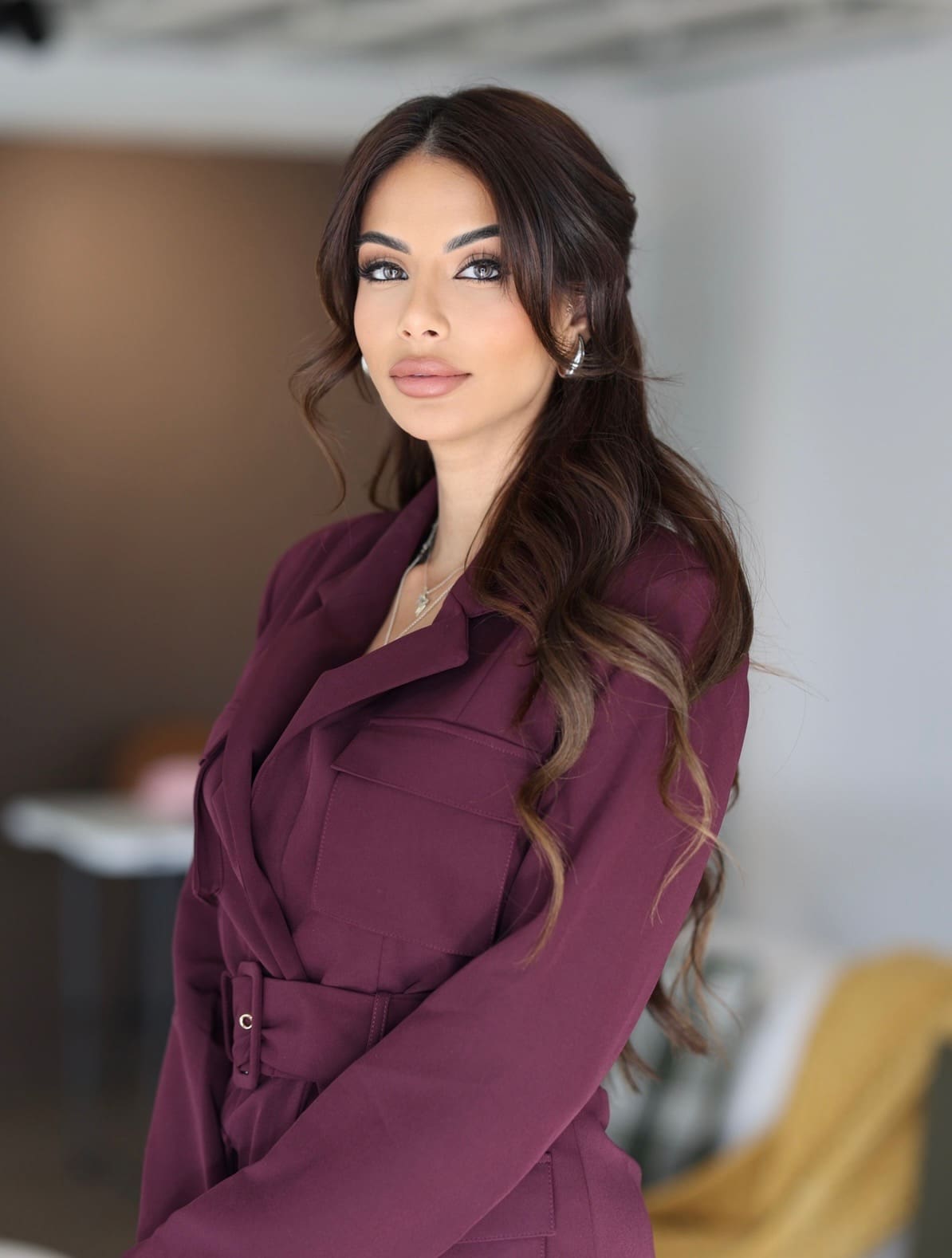 Side portrait of Meesha Moulton in a maroon blazer, conveying confidence and approachability in a modern professional office.