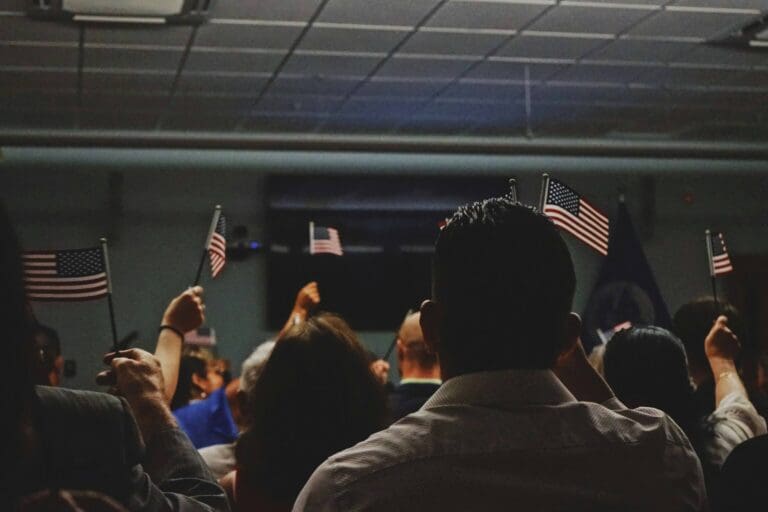 People holding small American flags during a citizenship or immigration-related event, representing lawful permanent resident status in the United States.